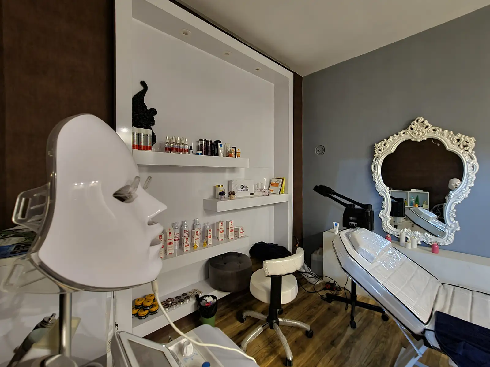 A facial treatment room with an LED face mask, a reclining bed, a steamer and shelves of skincare products
